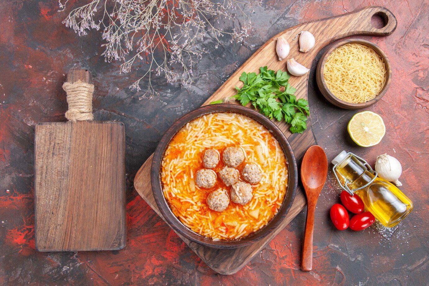meatballs-soup-with-noodles-board-uncooked-pastas-lemon-greens-oil-bottle-spoon-cutting-board-dark-table_140725-138381